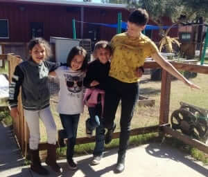 Emily and three students giggle and hold each other up while balancing on one foot. 