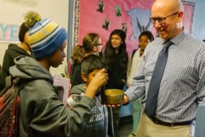 Brian Cooper stands in a school hallway and allows a student to ring his mindfulness bowl. 